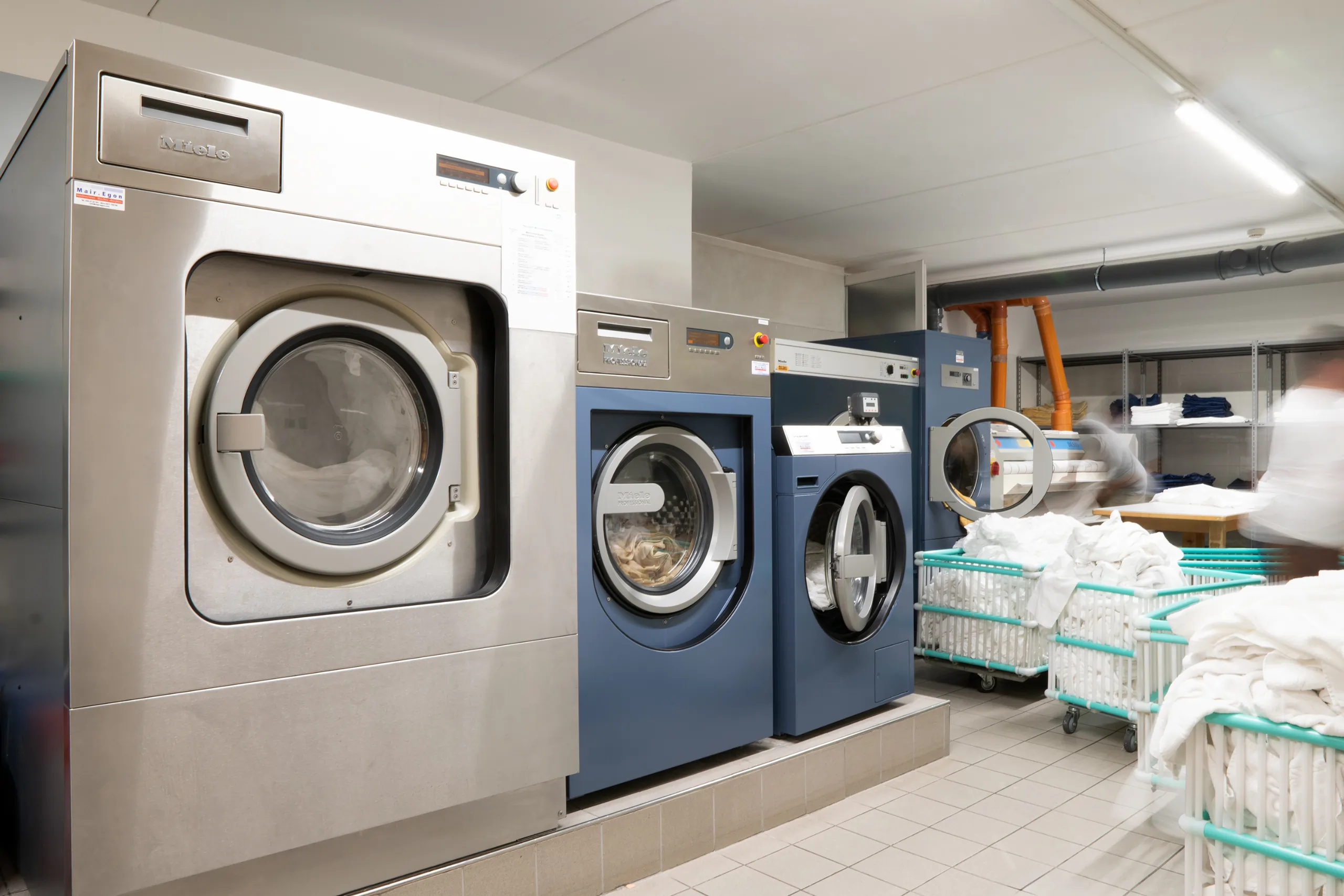 Eine Wäscherei mit einer silbernen und drei blauen Waschmaschinen und Trocknern von der Marke Miele.